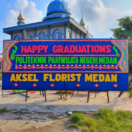 Papan bunga ucapan Happy Graduations Politeknik Pariwisata Negeri Medan dari Aksel Florist Medan dengan desain warna-warni cerah.